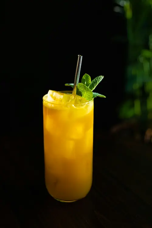 un cocktail création (long-drink) à la mangue et à la passion avec une tête de mente dans un verre collins
